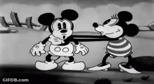 A Black And White Cartoon Of Mickey Mouse And Minnie Mouse Standing Next To Each Other On A Beach . GIF