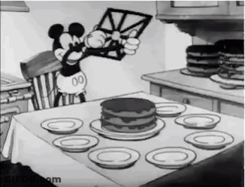A Black And White Cartoon Of Mickey Mouse Sitting At A Table With A Cake . GIF
