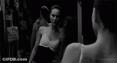 A Black And White Photo Of A Ballerina Looking At Herself In A Mirror . GIF