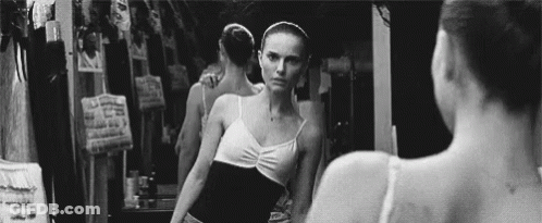 A Black And White Photo Of A Ballerina Looking At Herself In A Mirror . GIF