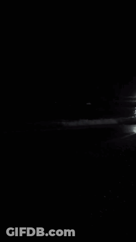 A Black And White Photo Of A Beach At Night With A Boat In The Distance GIF