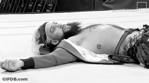 A Black And White Photo Of A Bearded Wrestler Laying On The Ground In A Wrestling Ring . GIF