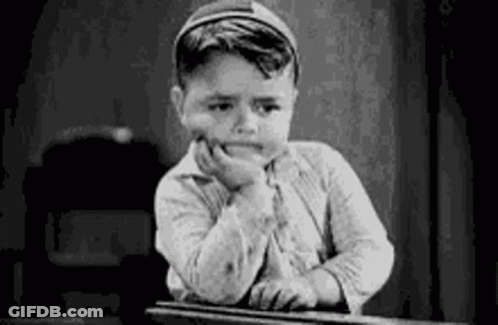 A Black And White Photo Of A Boy Sitting At A Desk With His Hand On His Chin . GIF