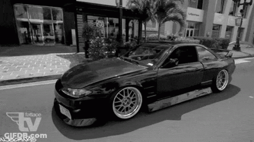 A Black And White Photo Of A Car On A City Street . GIF