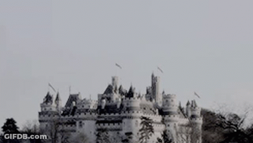 A Black And White Photo Of A Castle On A Hill With Birds Flying Around It . GIF