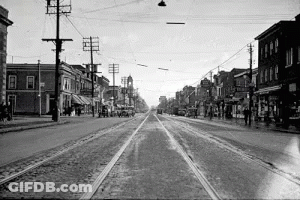 A Black And White Photo Of A City Street With A Train Going Down It GIF