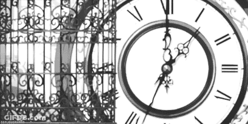 A Black And White Photo Of A Clock With Roman Numerals And A Fence In The Background . GIF