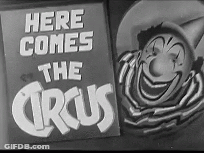 A Black And White Photo Of A Clown And A Sign That Says `` Here Comes The Circus '' GIF