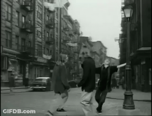 A Black And White Photo Of A Couple Walking Down A Street GIF