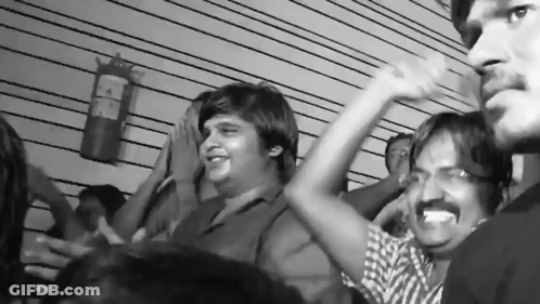 A Black And White Photo Of A Crowd With A Fire Extinguisher On The Wall Behind Them GIF