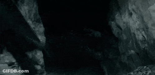 A Black And White Photo Of A Dragon Flying Over A Rocky Hillside . GIF