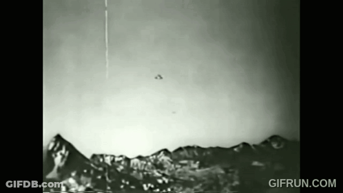 A Black And White Photo Of A Flying Object Over A Mountain Range . GIF