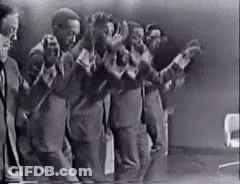 A Black And White Photo Of A Group Of Men Standing Next To Each Other In A Room . GIF