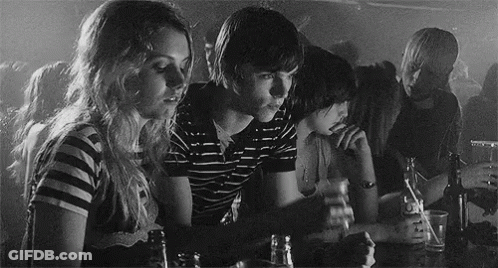 A Black And White Photo Of A Group Of People Sitting At A Table Drinking Beer GIF