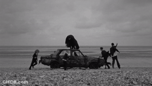 A Black And White Photo Of A Group Of People Standing Around A Car GIF