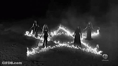 A Black And White Photo Of A Group Of Women Standing Around A Fire . GIF