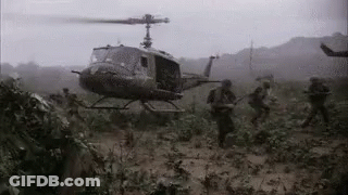 A Black And White Photo Of A Helicopter Flying Over A Field Of Soldiers GIF