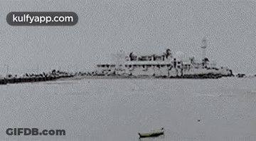 A Black And White Photo Of A Large Ship In The Ocean With A Boat In The Foreground . GIF