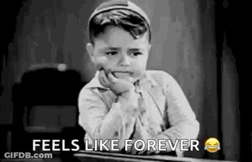 A Black And White Photo Of A Little Boy Sitting At A Desk With His Hand On His Face . GIF