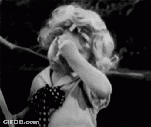 A Black And White Photo Of A Little Girl Covering Her Face With Her Hands . GIF