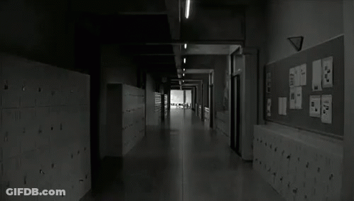 A Black And White Photo Of A Long Hallway In A School With Lockers And A Bulletin Board . GIF