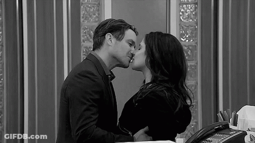 A Black And White Photo Of A Man And A Woman Kissing In An Office . GIF