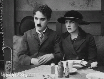 A Black And White Photo Of A Man And A Woman Sitting At A Table . GIF