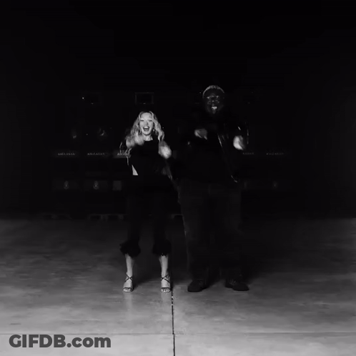 A Black And White Photo Of A Man And Woman Dancing In Front Of A Row Of Bellway Trucks GIF