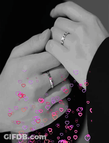 A Black And White Photo Of A Man And Woman Holding Hands With Hearts Flying Around Them GIF