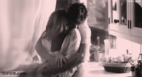A Black And White Photo Of A Man And Woman Hugging In A Kitchen . GIF