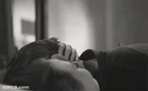A Black And White Photo Of A Man And Woman Laying On A Bed . The Woman Is Wearing A Ring On Her Finger . GIF