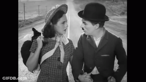 A Black And White Photo Of A Man And Woman Standing Next To Each Other GIF