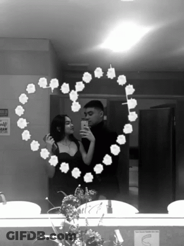 A Black And White Photo Of A Man And Woman Taking A Selfie In A Bathroom Mirror GIF