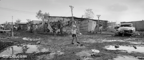 A Black And White Photo Of A Man Carrying A Bucket Of Water In A Muddy Area . GIF