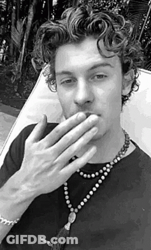 A Black And White Photo Of A Man Covering His Mouth With His Hands While Wearing A Necklace . GIF