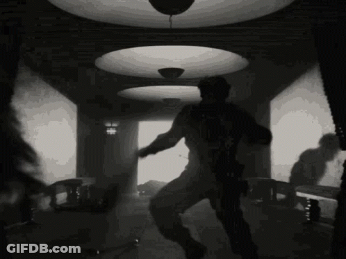 A Black And White Photo Of A Man Dancing In A Room With A Ceiling Light . GIF