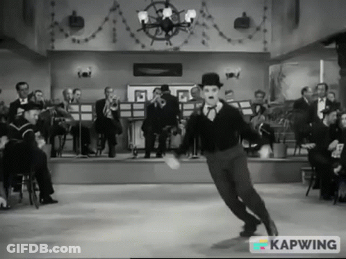 A Black And White Photo Of A Man Dancing In Front Of An Orchestra With Kapwing In The Corner GIF