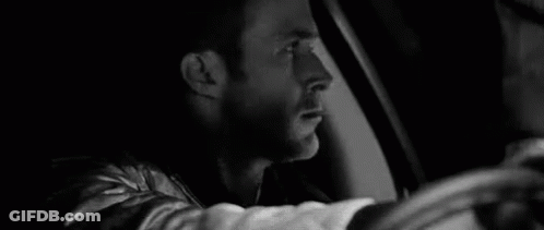 A Black And White Photo Of A Man Driving A Car At Night . GIF