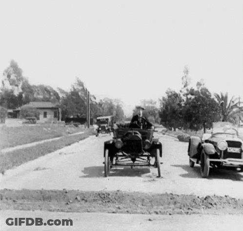 A Black And White Photo Of A Man Driving An Old Car GIF