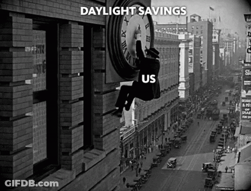 A Black And White Photo Of A Man Hanging From A Clock That Says Daylight Savings Us GIF