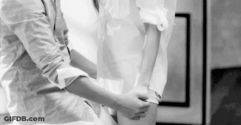 A Black And White Photo Of A Man Helping A Woman Tie Her Shirt . GIF