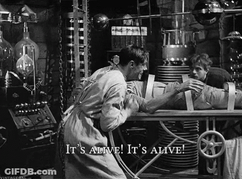 A Black And White Photo Of A Man Holding A Mummy With The Caption It 'S Alive It 'S Alive GIF
