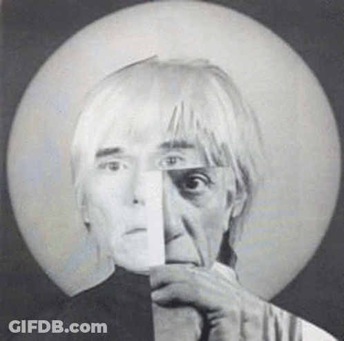 A Black And White Photo Of A Man Holding A Piece Of Paper To His Face GIF