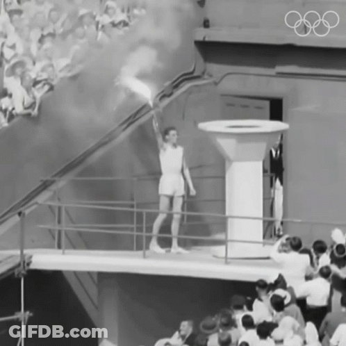 A Black And White Photo Of A Man Holding A Torch With The Olympic Rings On The Wall Behind Him GIF