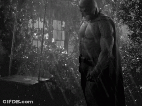 A Black And White Photo Of A Man In A Batman Costume Standing In Front Of A Window . GIF