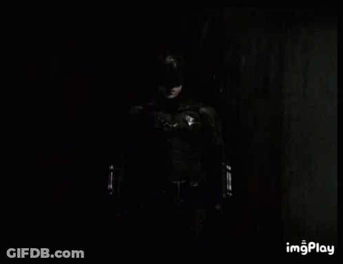 A Black And White Photo Of A Man In A Batman Costume Standing In The Dark . GIF
