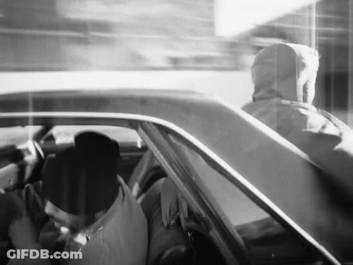 A Black And White Photo Of A Man In A Hoodie Driving A Car GIF