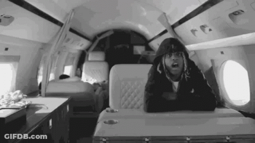 A Black And White Photo Of A Man In A Hoodie Sitting On A Plane . GIF