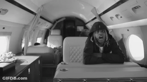 A Black And White Photo Of A Man In A Hoodie Sitting On A Plane GIF