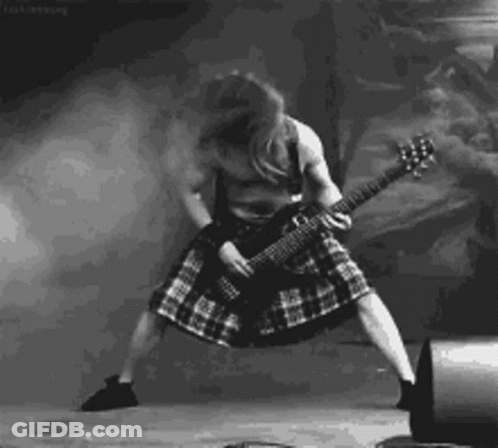 A Black And White Photo Of A Man In A Kilt Playing A Guitar On Stage . GIF